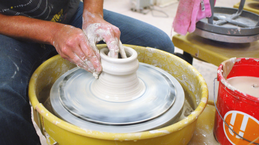 Close up of hands on shaping a white clay body spinning on a wheel.