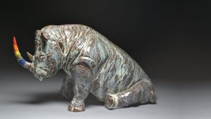 Ceramic rhinoceros with grey textured skin and rainbow horn, by Mac McCusker.
