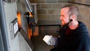Mac McCusker holds a brick while facing the gas kiln on profile.