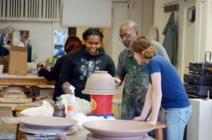 Three people examine the details of an upside down bowl in the ceramics studio.