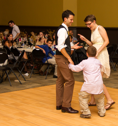 A couple and a kid dancing on the Union Project dance floor with guests in the background