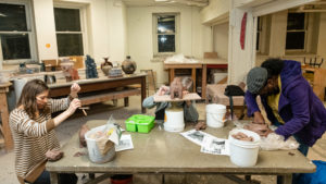 Students with masks on work on their individual pieces in the ceramics studio.
