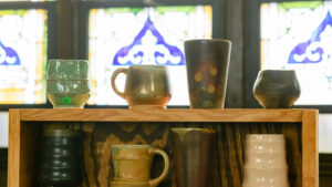 Close up of various ceramic cups with stained glass in the background.