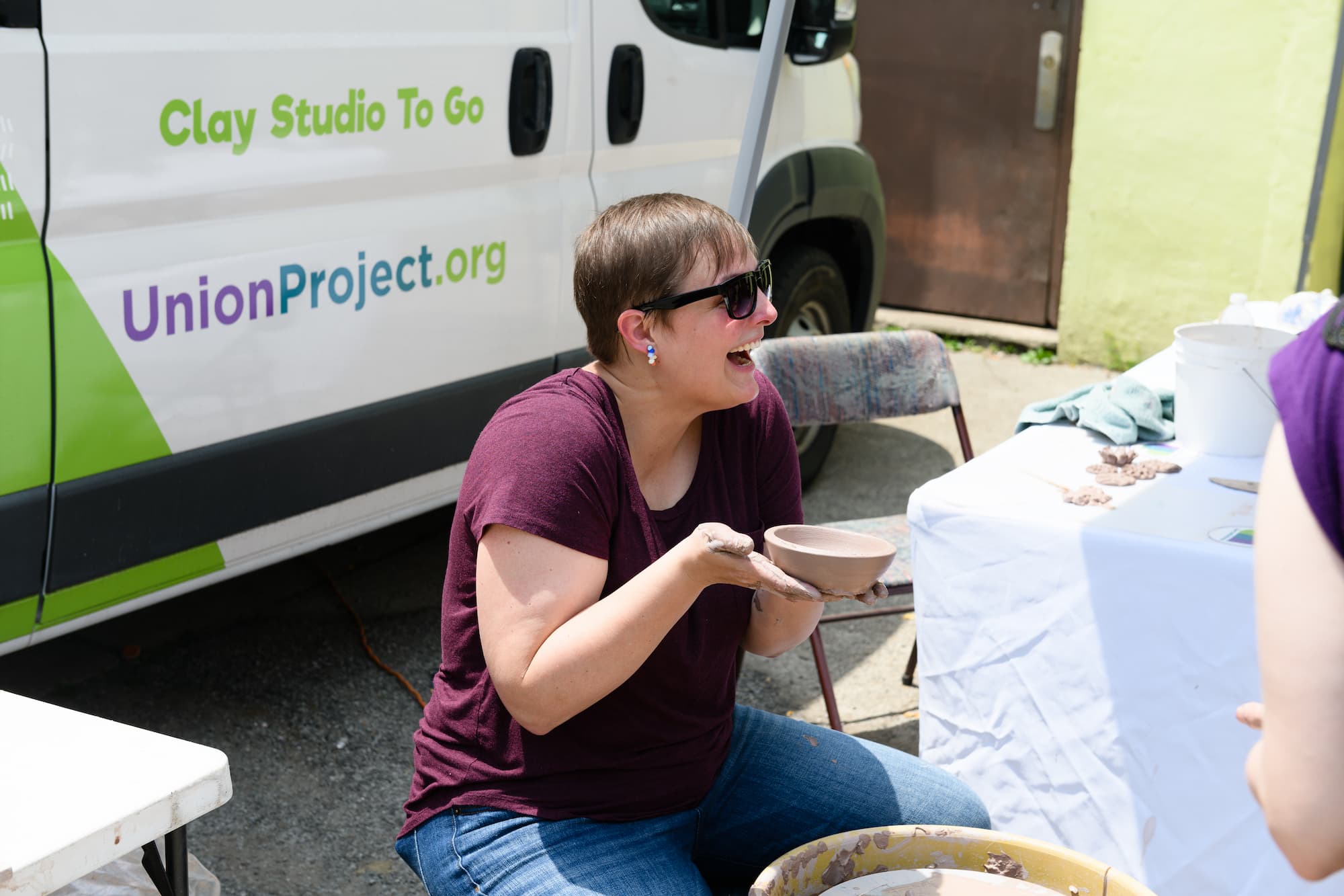 Student holds up clay bowl smiling outside the Wheel Mobile.